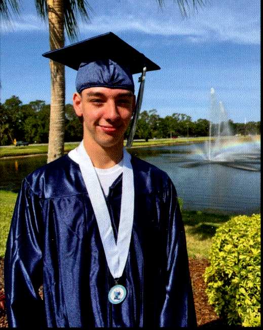 My nephew Maxwell on his high school graduation day, dressed in his cap and gown by a peaceful pond with a fountain.