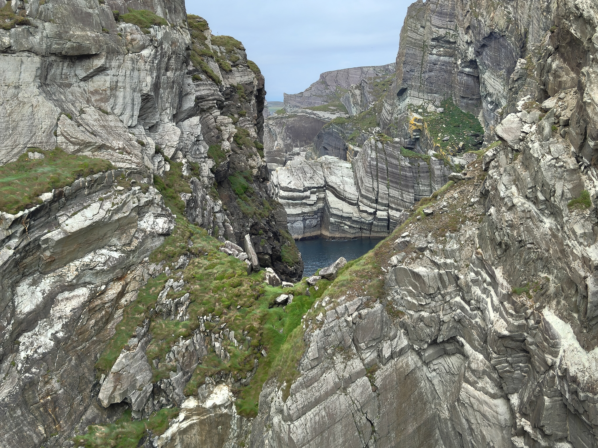 A complex set of rock layers with a glimpse of a bay enclosed by more sheer cliffs
