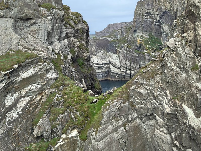 A complex set of rock layers with a glimpse of a bay enclosed by more sheer cliffs