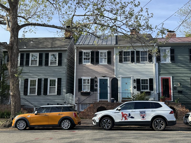 an orange mini and a white VW Tiguan parallel parked on the street in front of a row of historical townhomes.