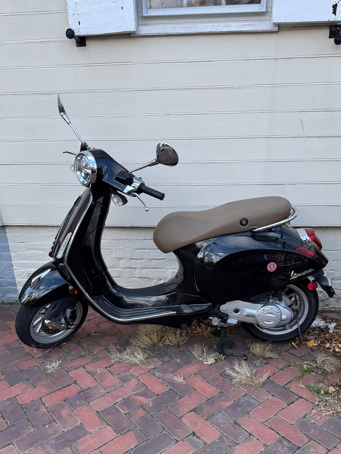 black moped parked on a brick sidewalk in front of a townhouse