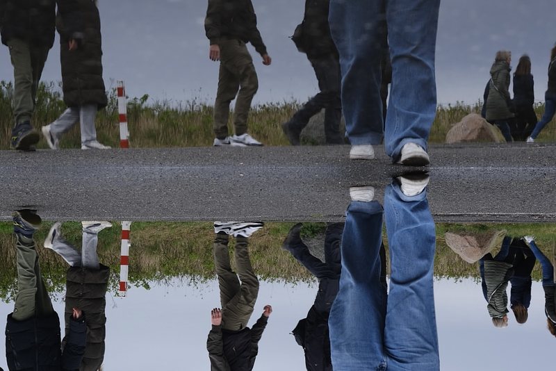 5 pairs of legs walking by, one pair walking towards the photographer. Everything is reflected in a puddle. The picture is turned upside down.