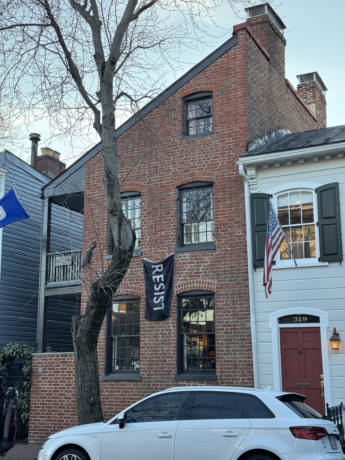 brick townhome with a slanted "flounder" style roof. black flag with white letters that read "resist" hangs from the side of the house