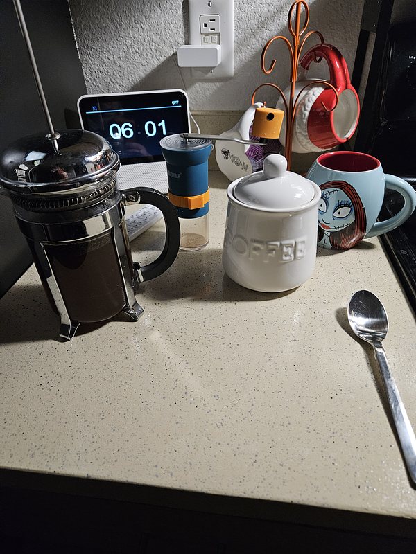 Picture of a kitchen counter with a jar that says "coffee", a French press coffee roaster with fresh coffee, and a coffee cup.