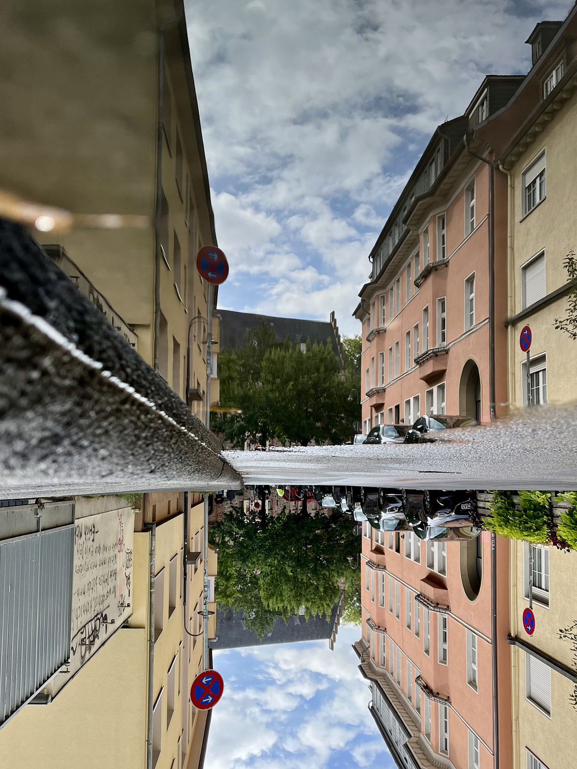 Street with yellow and orange-red three storey buildings, reflected in a puddle on the asphalt. The whole picture is turned upsidedown.
