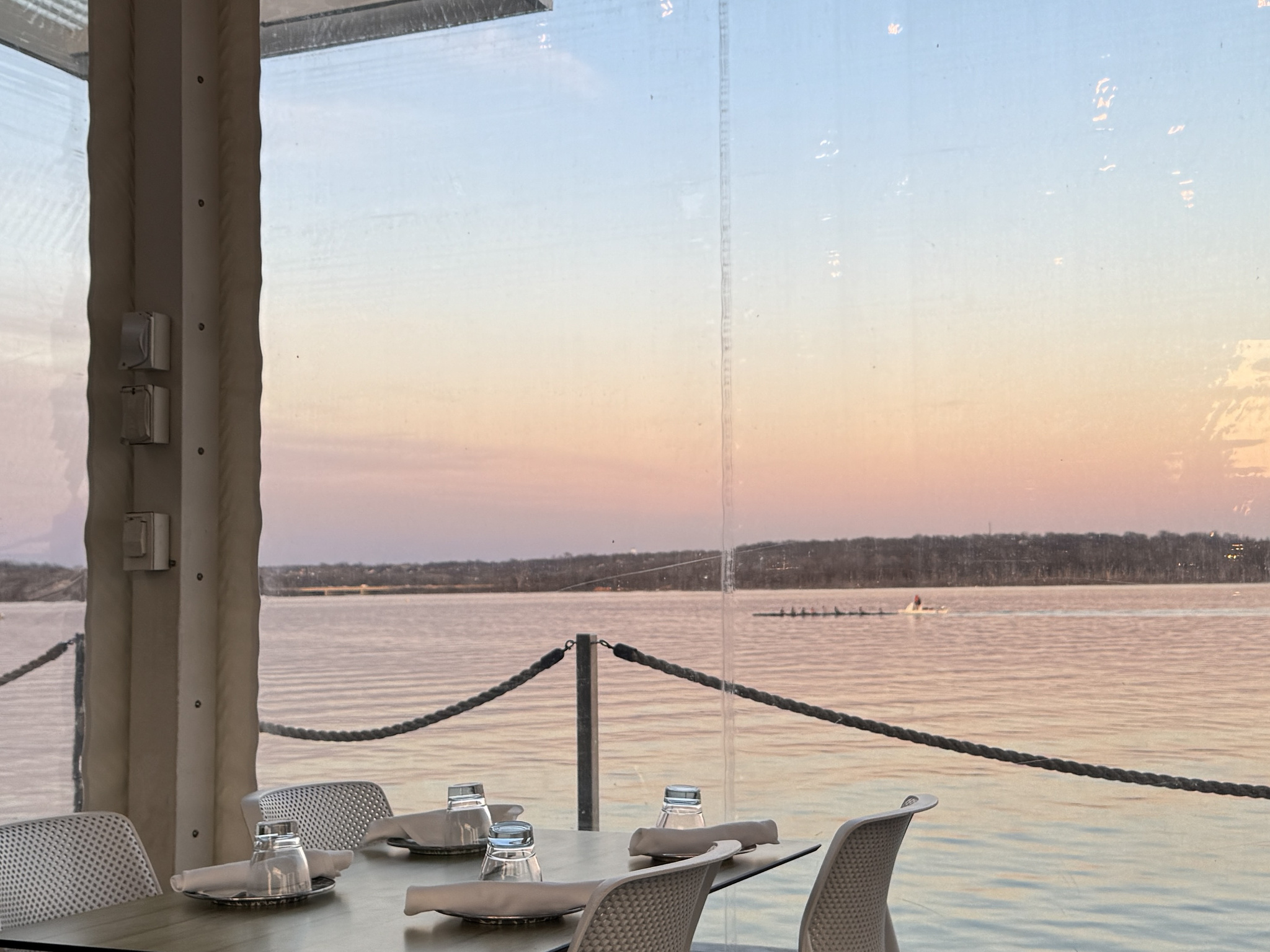 restaurant table and chairs with the Potomac River in the background. peach colored sunset sky. crew boat on the water