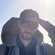 It's me, holding my cap in the wind. Wearing sunglasses. Short beard, slight smile. Sun in my back.