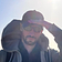 It's me, holding my cap in the wind. Wearing sunglasses. Short beard, slight smile. Sun in my back.