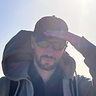 It's me, holding my cap in the wind. Wearing sunglasses. Short beard, slight smile. Sun in my back.