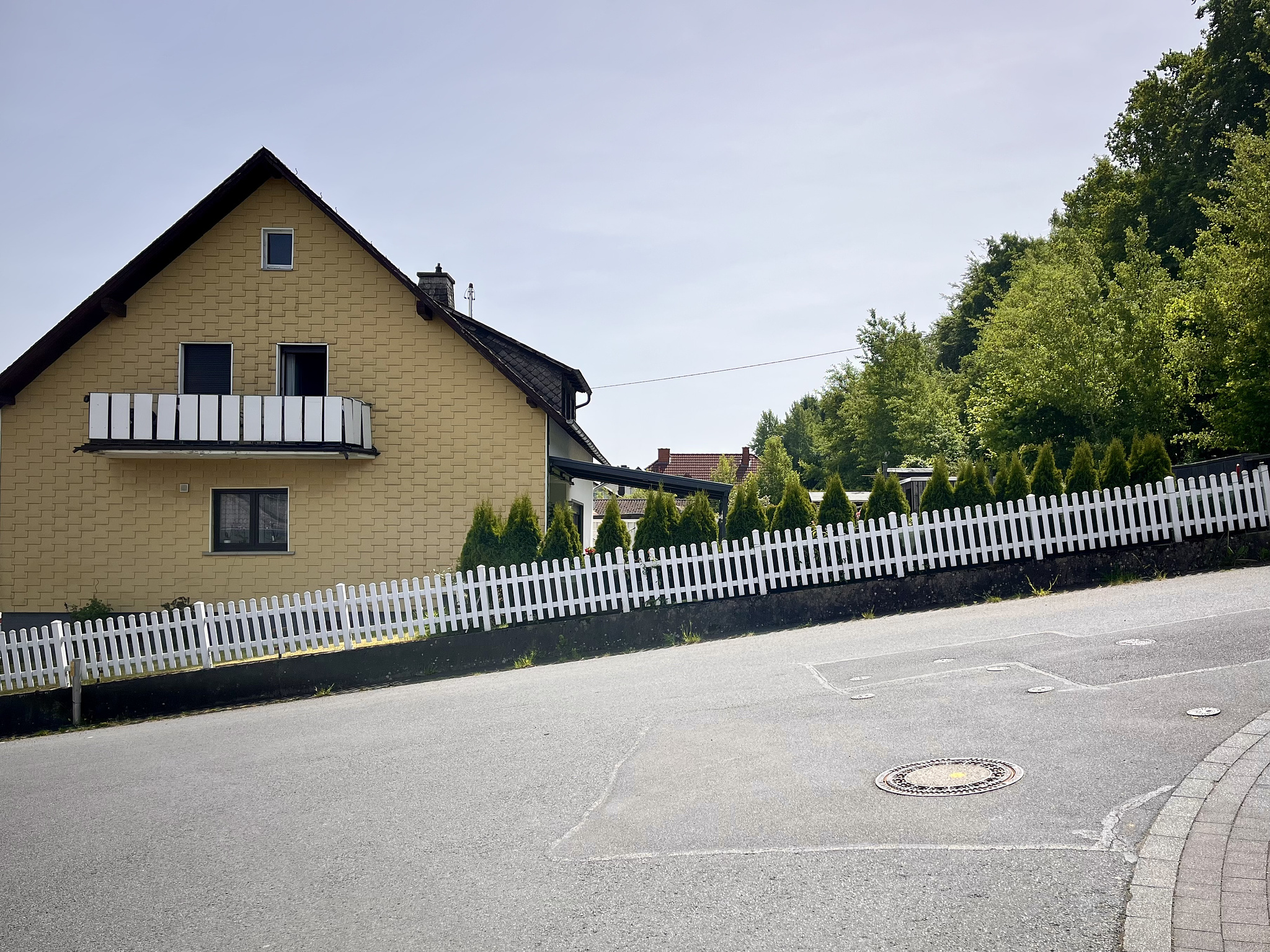 a yellow house built at a hill. in front of hhr house there is a white, medium-sized fence, looking slanted, as it is build along thd hill.