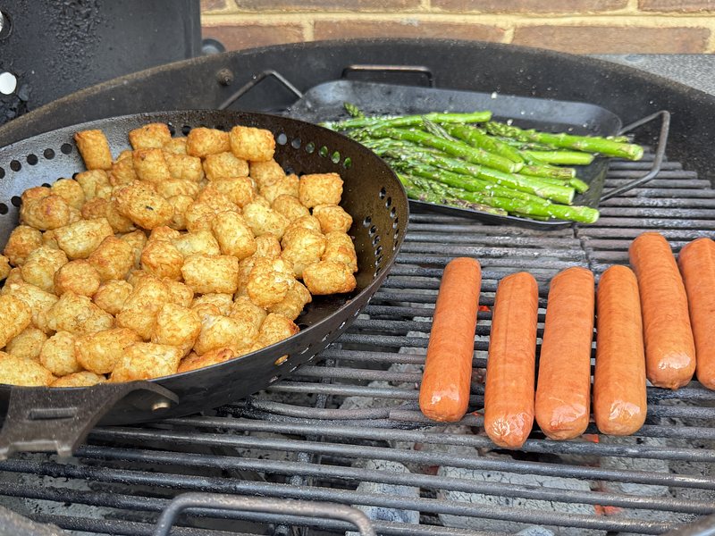 hot dogs, asparagus, and tater tots arranged on a charcoal grill