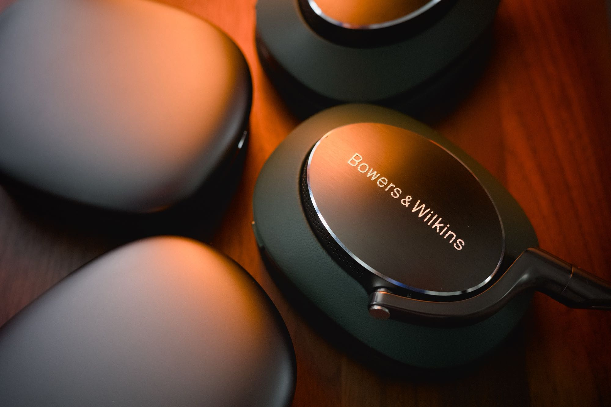 Close up of the Px8 and Apple AirPods Max lying flat on a walnut surface, earcups nearly touching, bathed in an orange light.