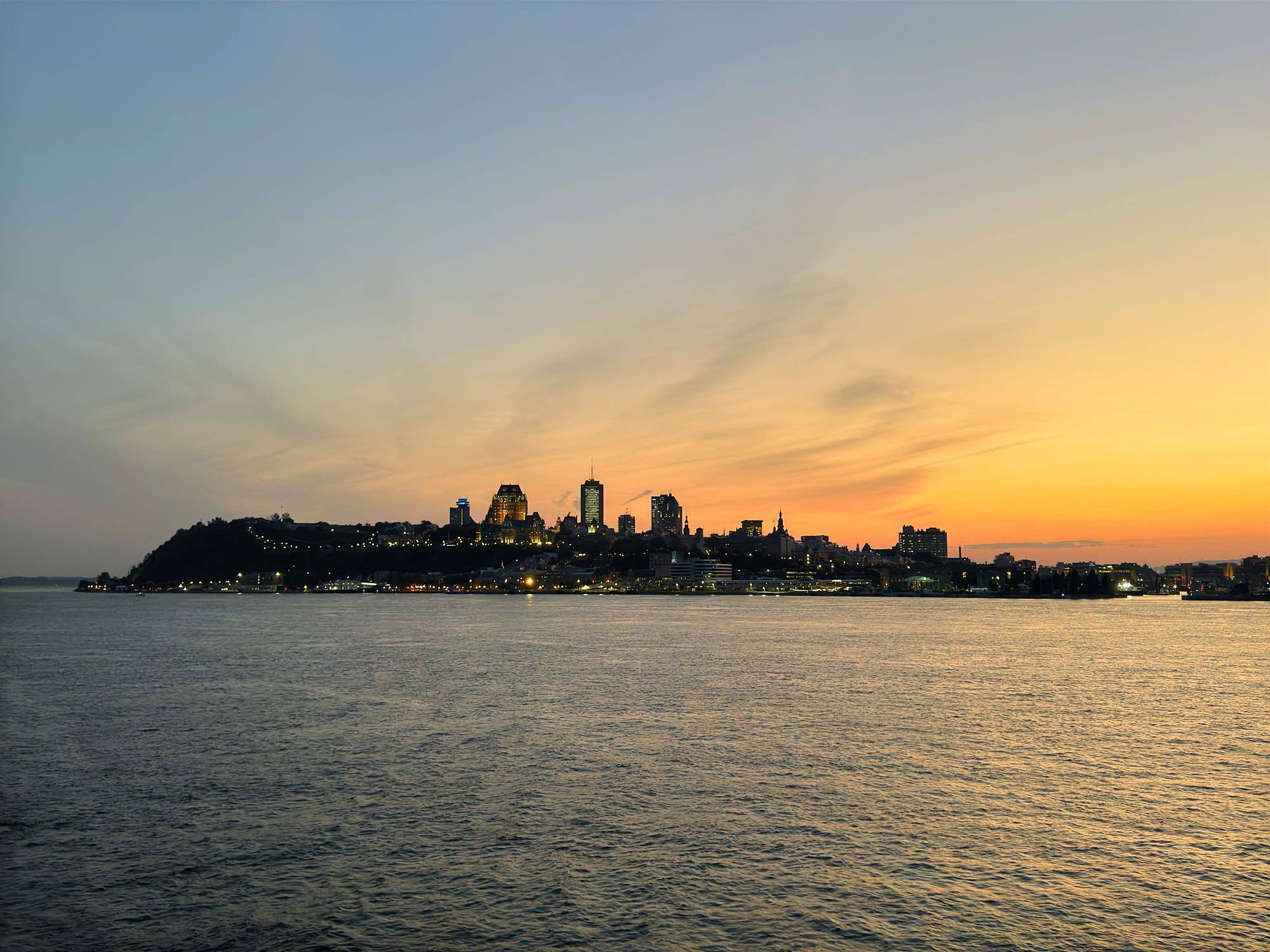 A vibrant sunset view of downtown Quebec City, as viewed from a ship passing by on the river.