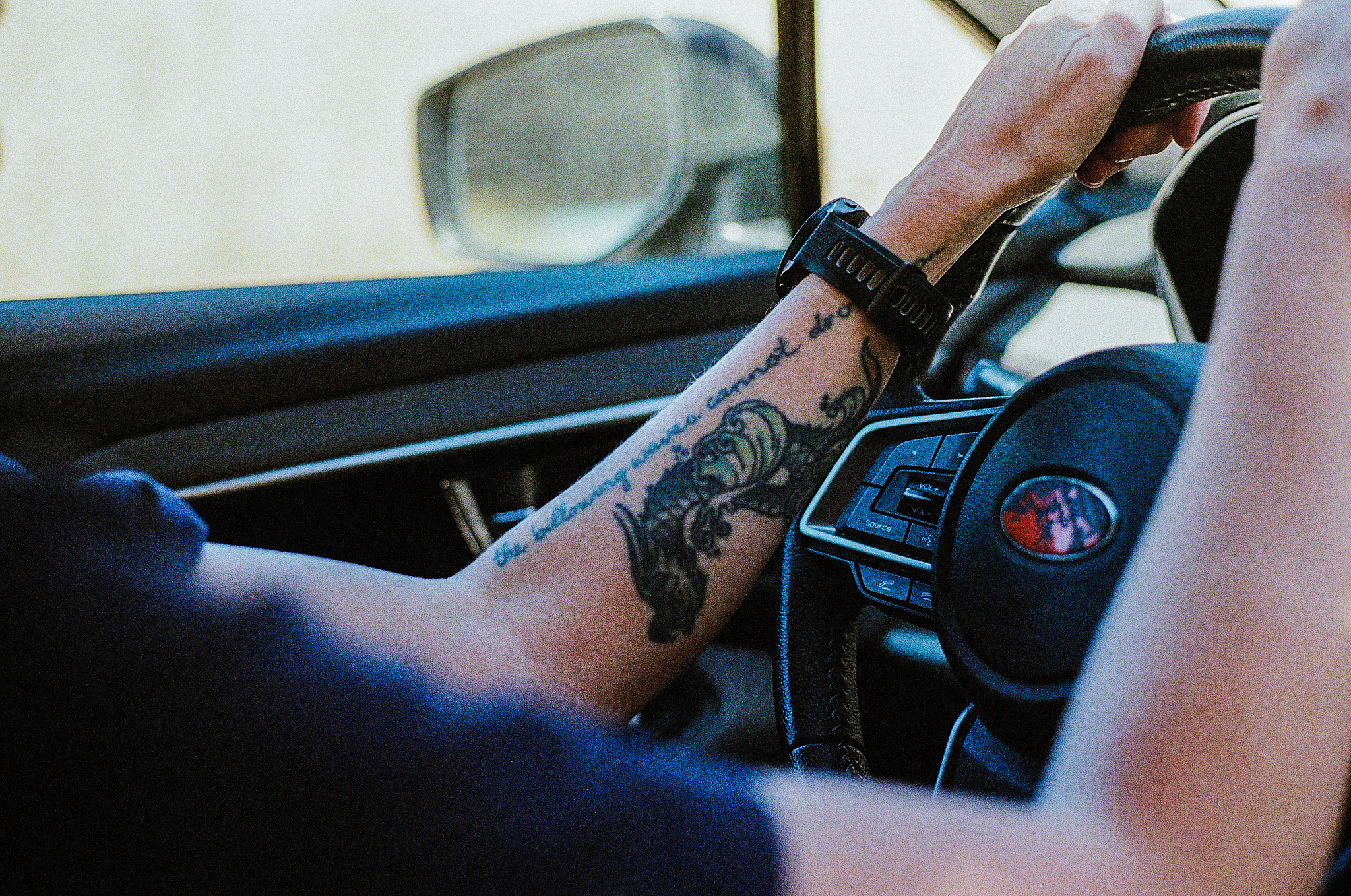 A woman's tatooed forearm and a steering wheel.