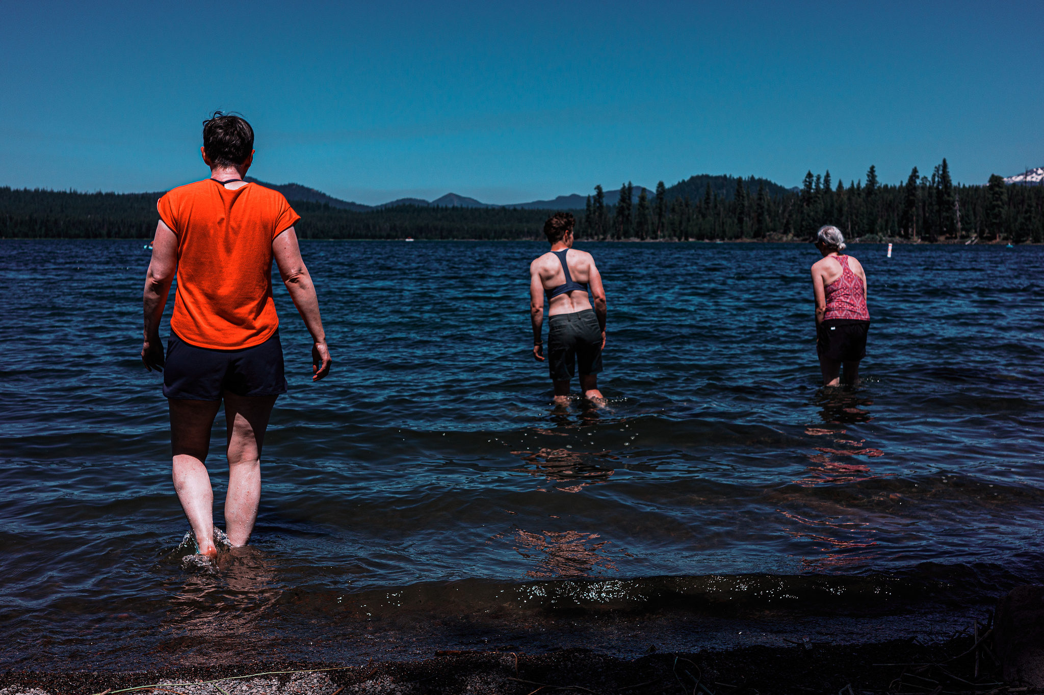 Three women wade in a mountain lake under a blue sky