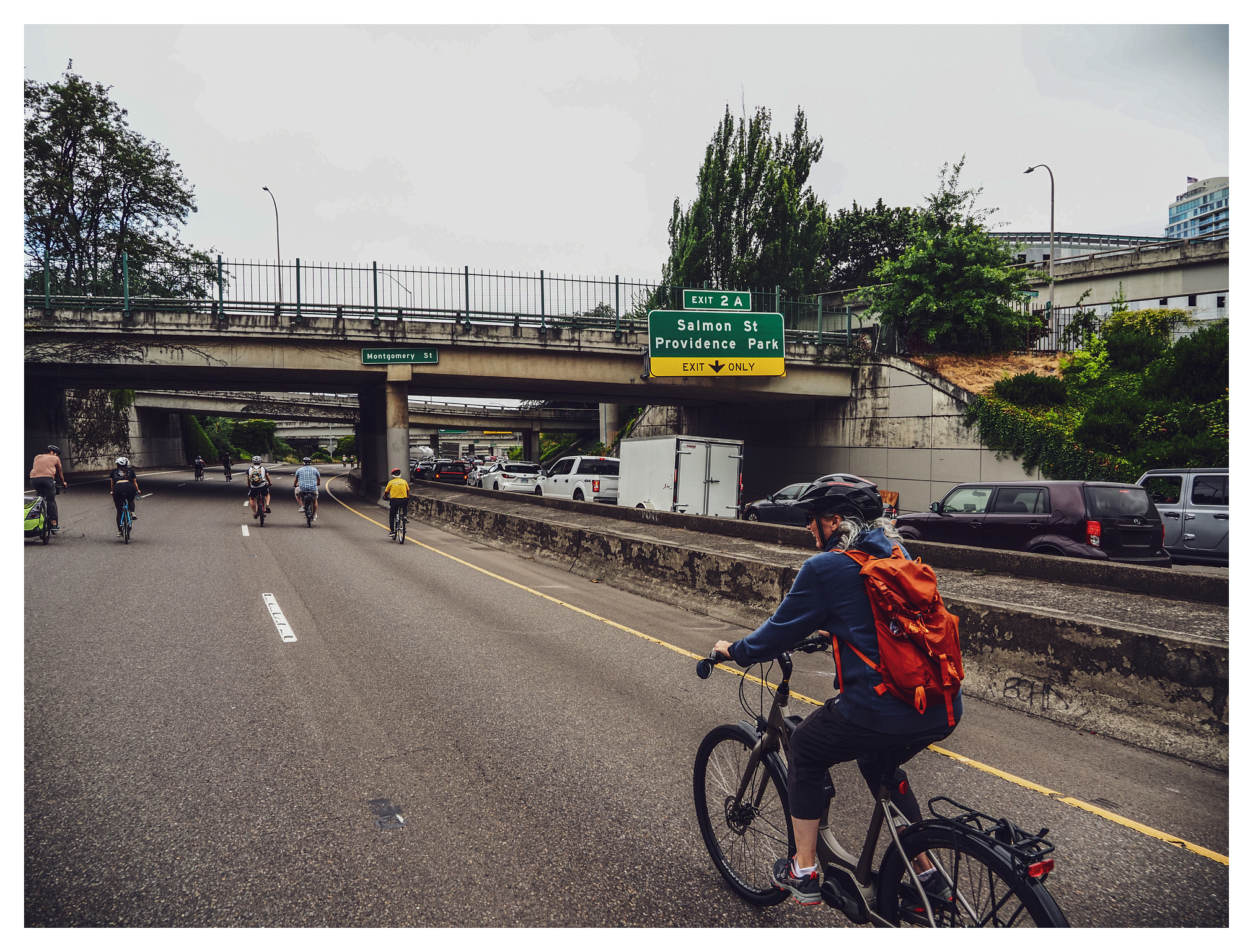 Bicyclists pedaling past stopped traffic on the other side of a half-closed freeway.