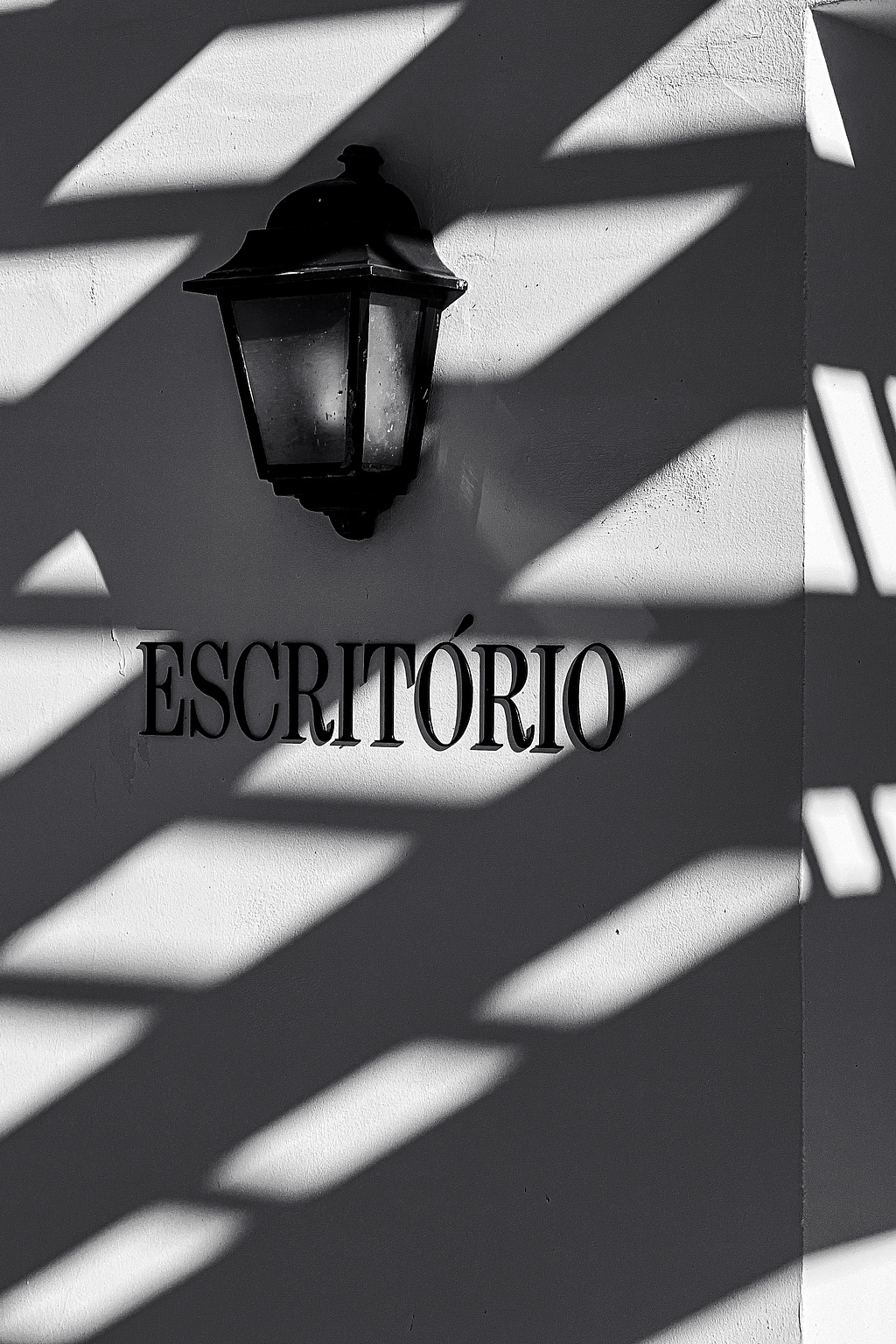 The word "Escritório" (Office), on a wall, with a lamp over it. Shadows. 