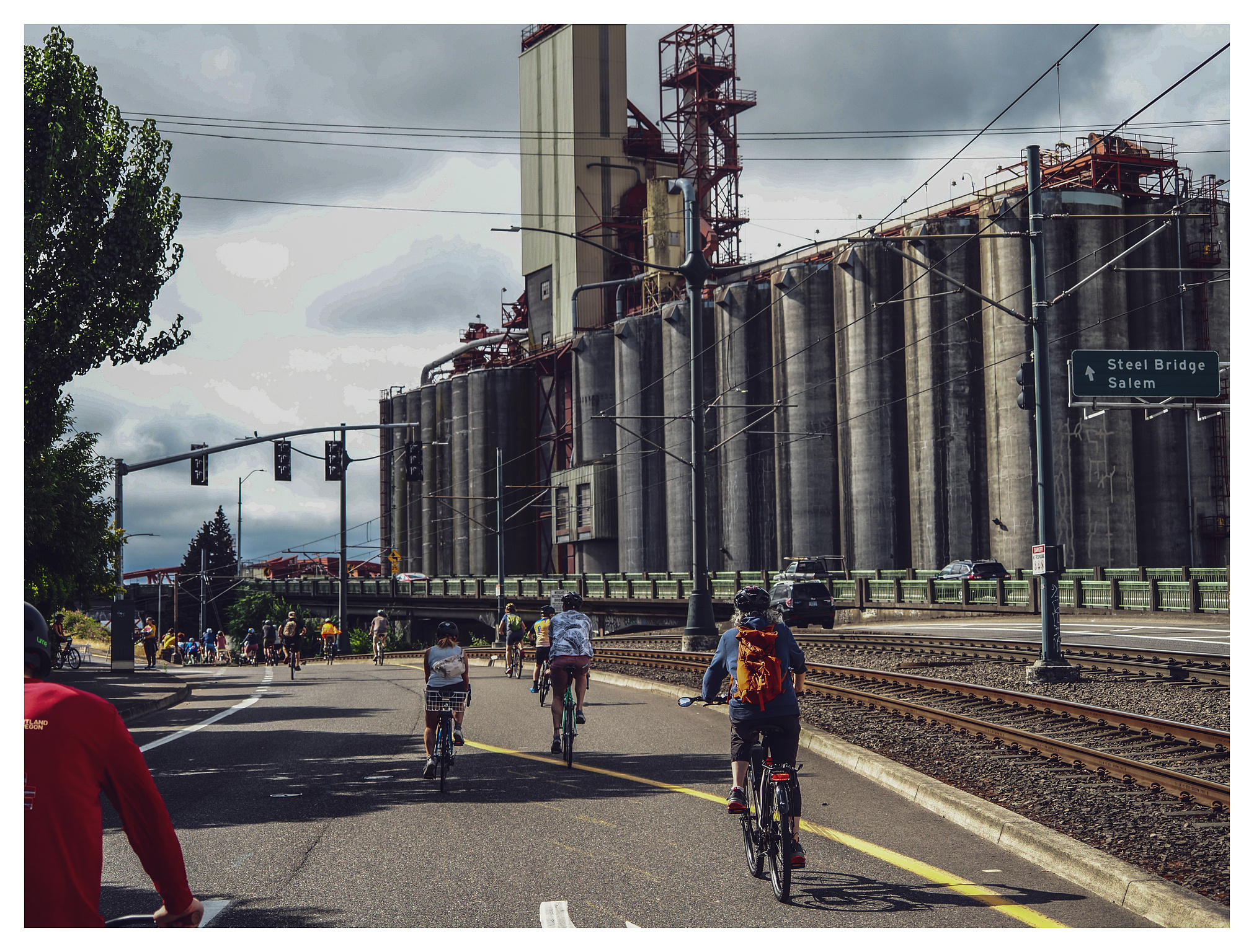 Bicylclists pedaling past storage silos. 