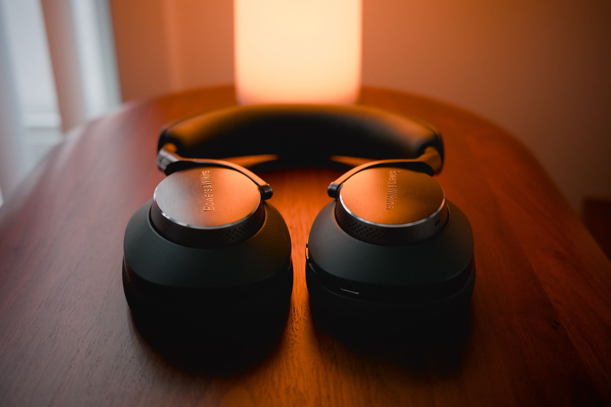 Head-on, low-angle view of the Px8 sitting on a walnut side table with a cylindrical orange light casting a warm glow over them.