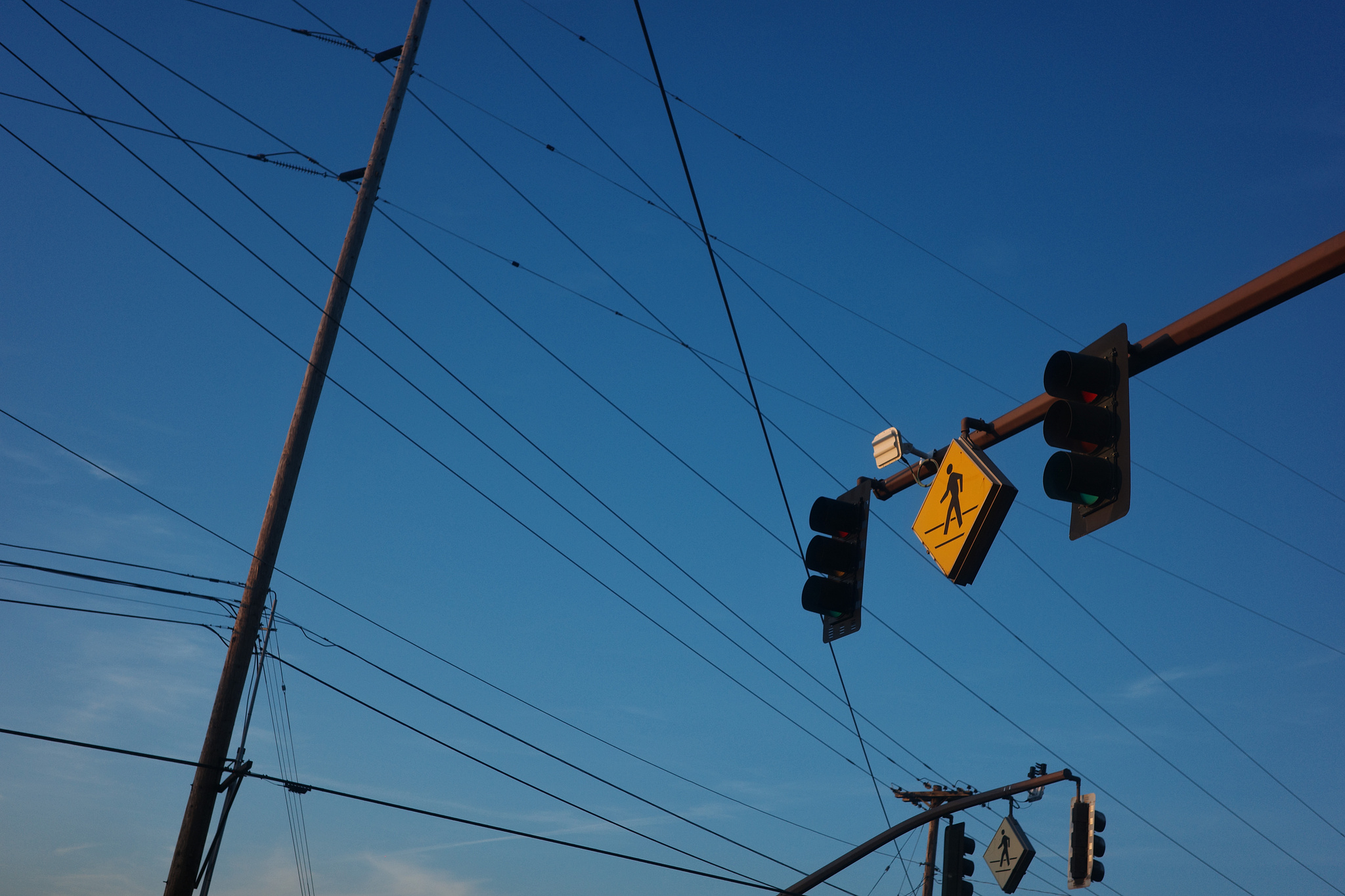 Traffic lights and a yellow pedestrian crossing sign against a blue sky