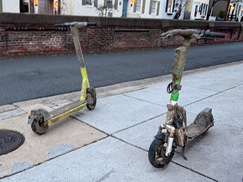 two very dirty electric scooters on the sidewalk