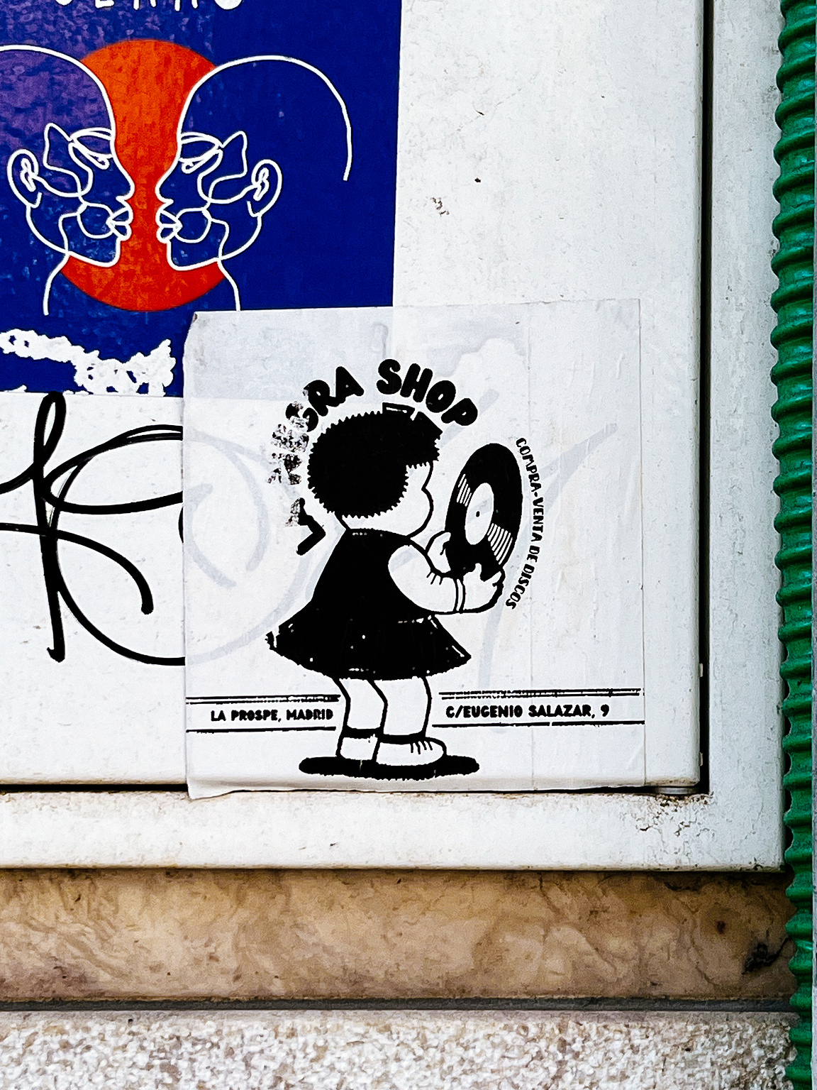 Sticker of a cartoon-style silhouette of a girl with a record on a tiled wall, among other street art pieces.