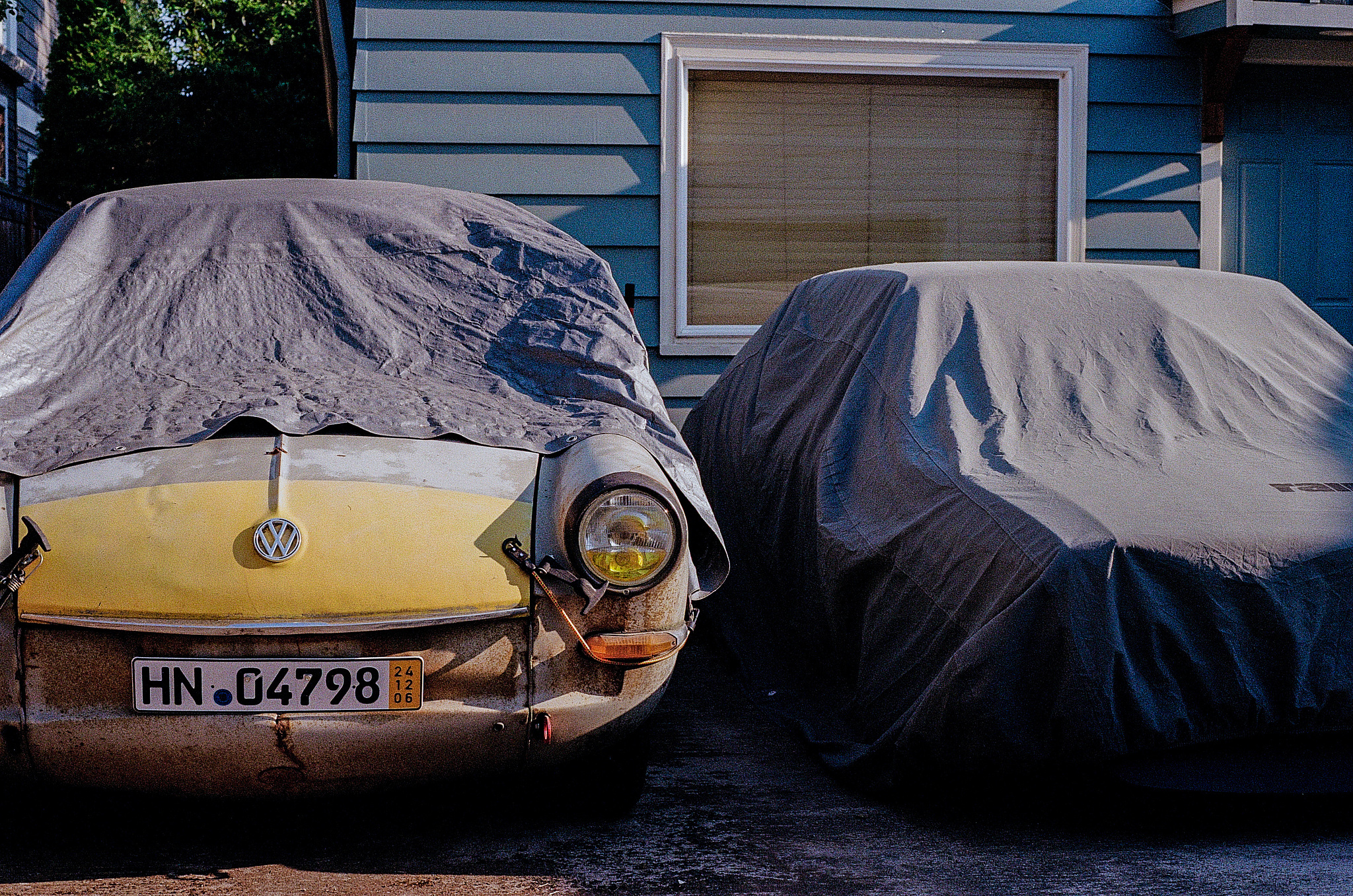 A yellow Volkswagen Karmen Ghia under a tarp in an alley