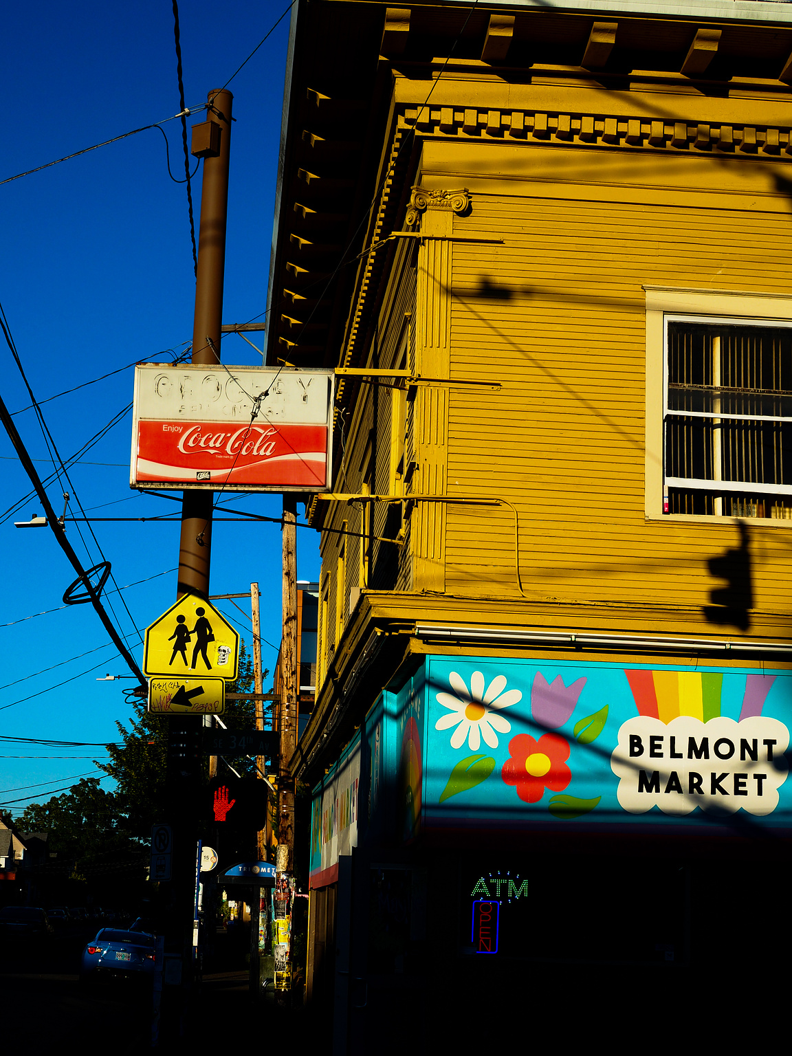 A store painted yellow with a faded Coca Cola sign and a colorful mural that reads "Belmont Market"