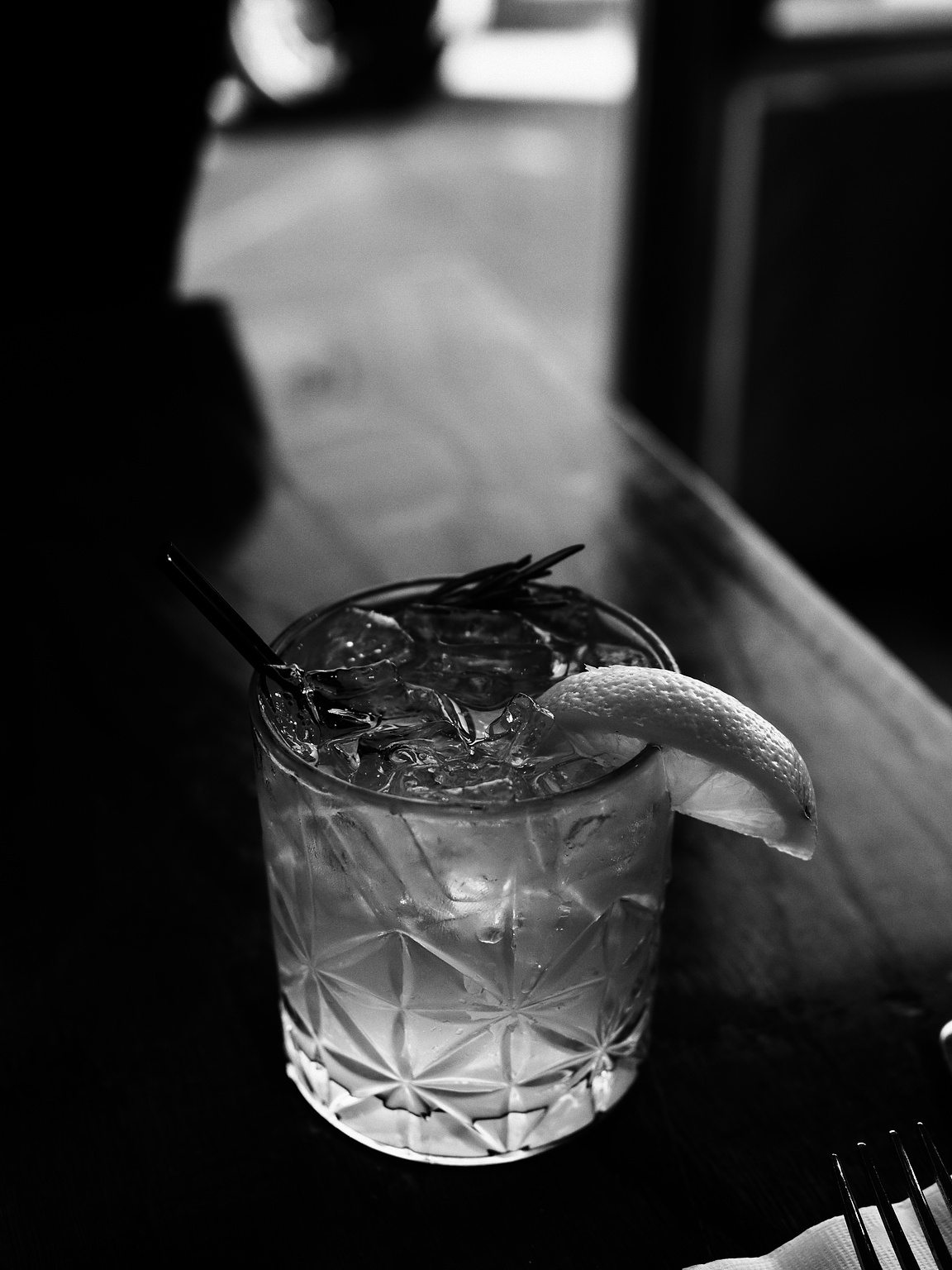 Monochrome photo of a cocktail in a cut glass tumbler with a sprig of rosemary and a twist