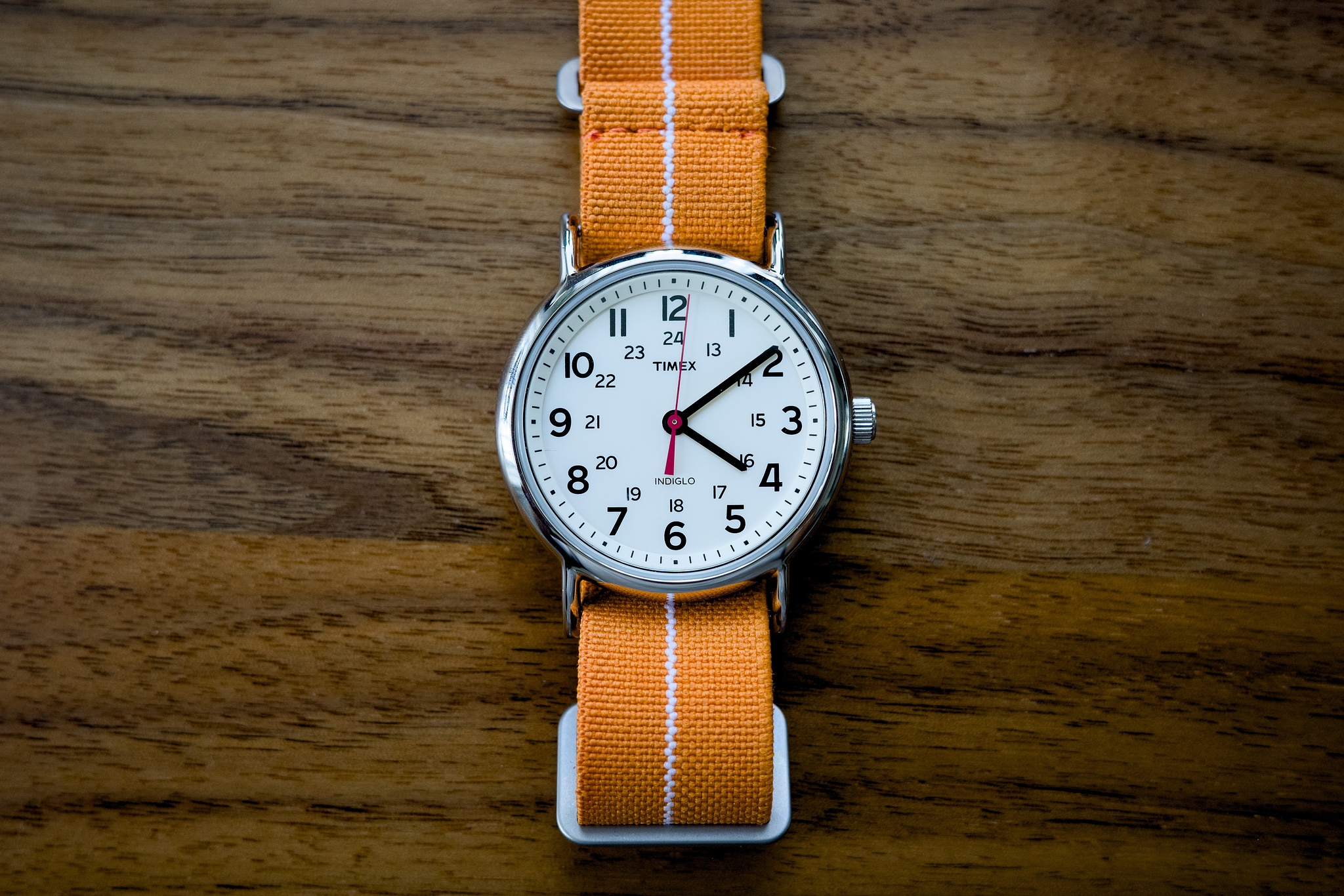 A 38mm Timex Weekender on a walnut desktop, with a bright orange strap.