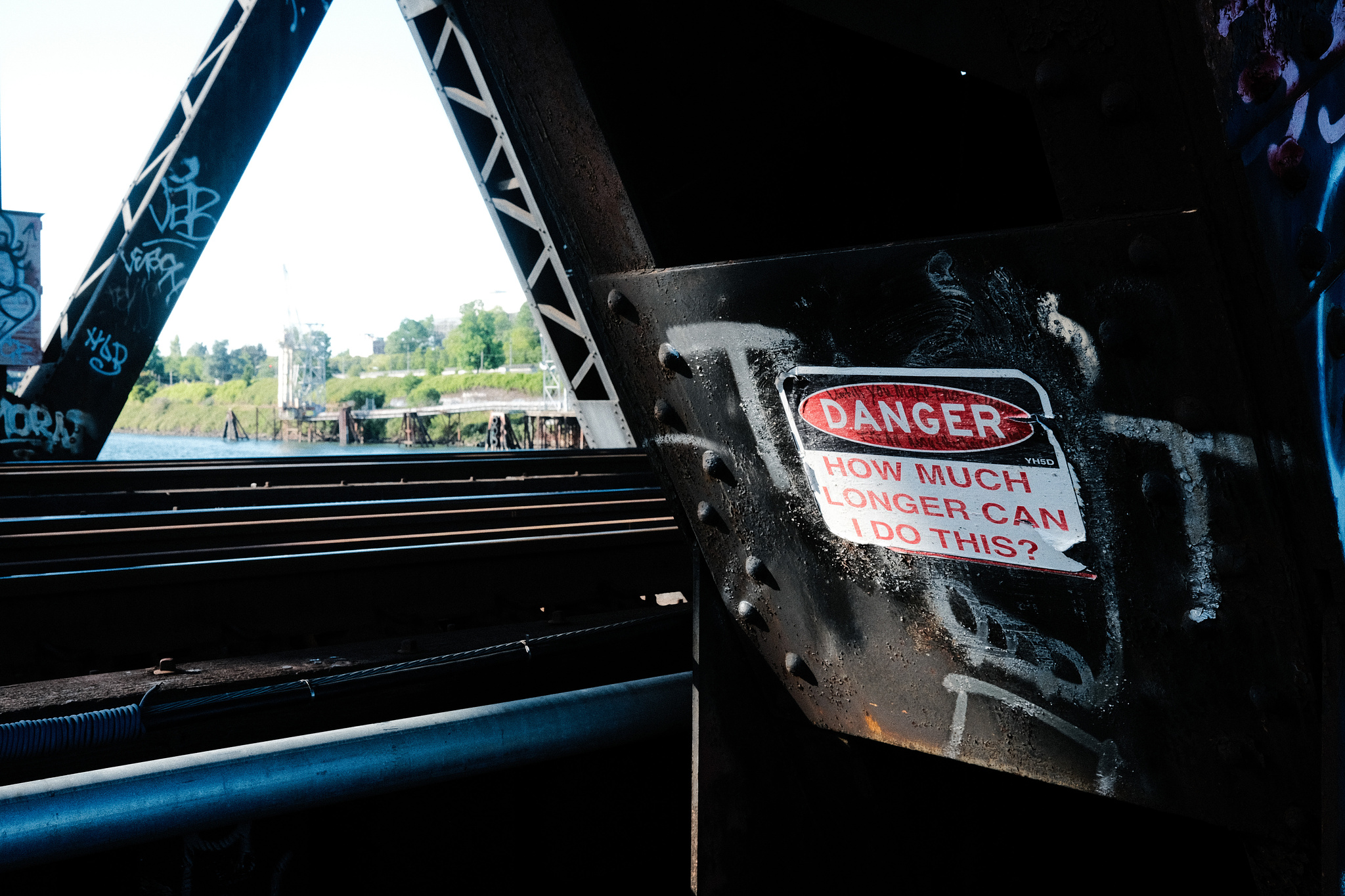 A sign wheatpasted to a steel girder that reads "DANGER: How much longer can I do this?"