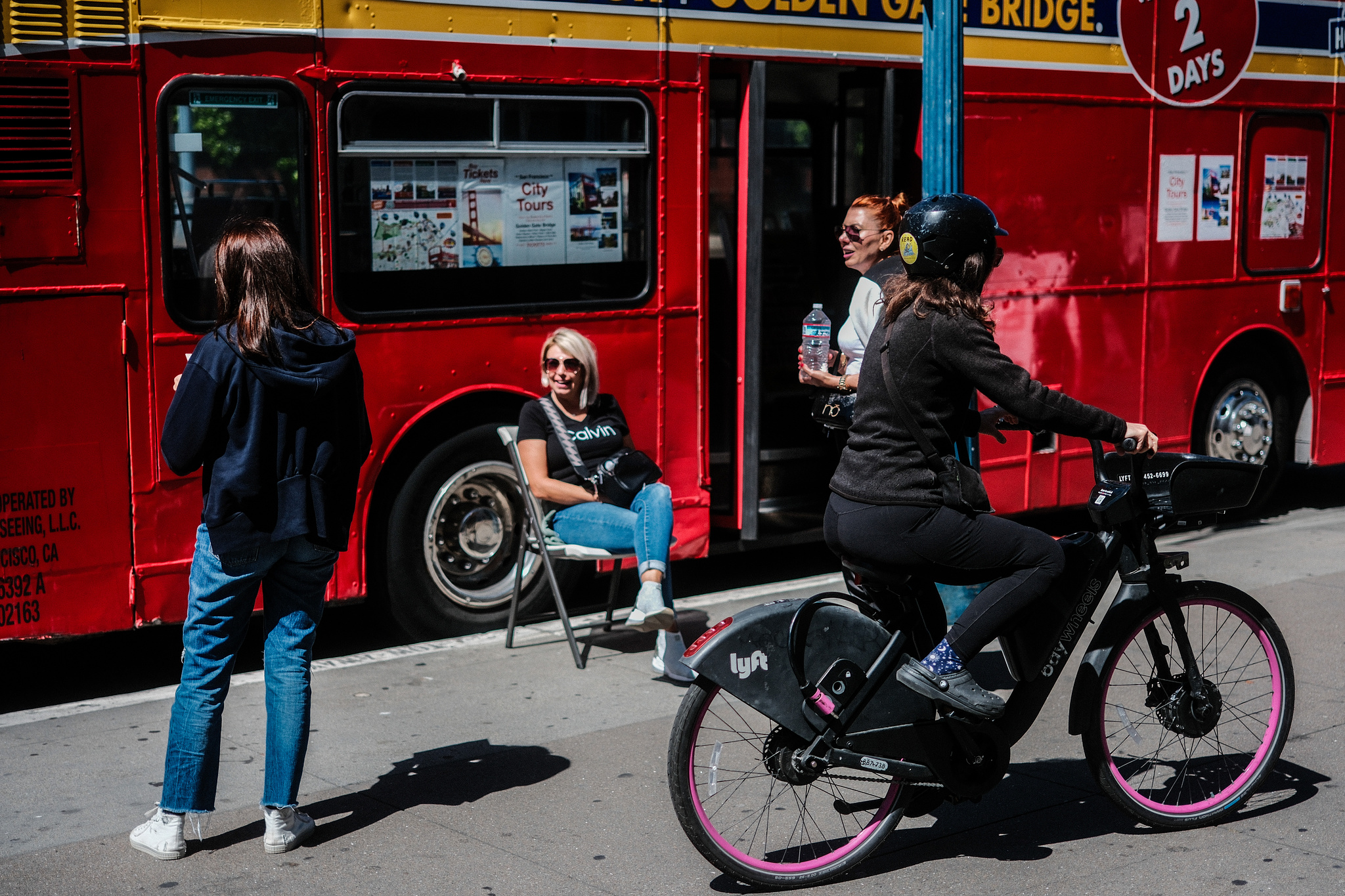 People on the sidewalk in front of a bright red tour bus