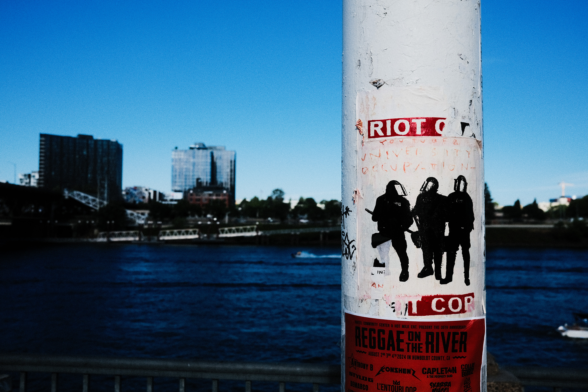 A red and white wheapaste on a white pole depicting riot cops. 