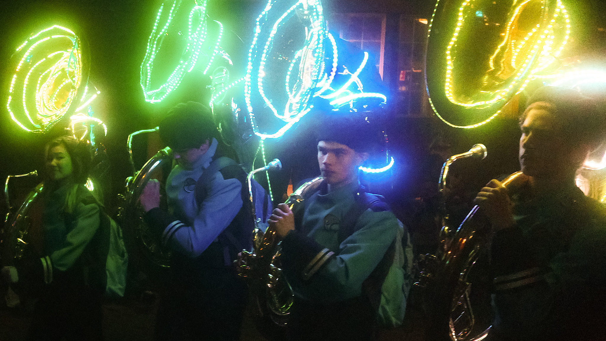 Tuba players with light-festooned instruments march in the dark