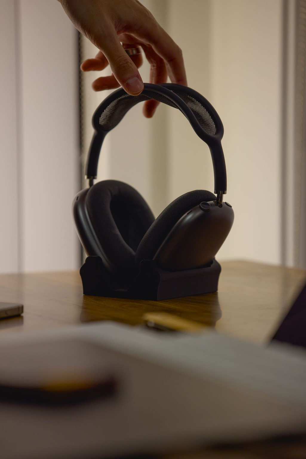 A hand reaches down to grab the AirPods Max from their desktop cradle stand.