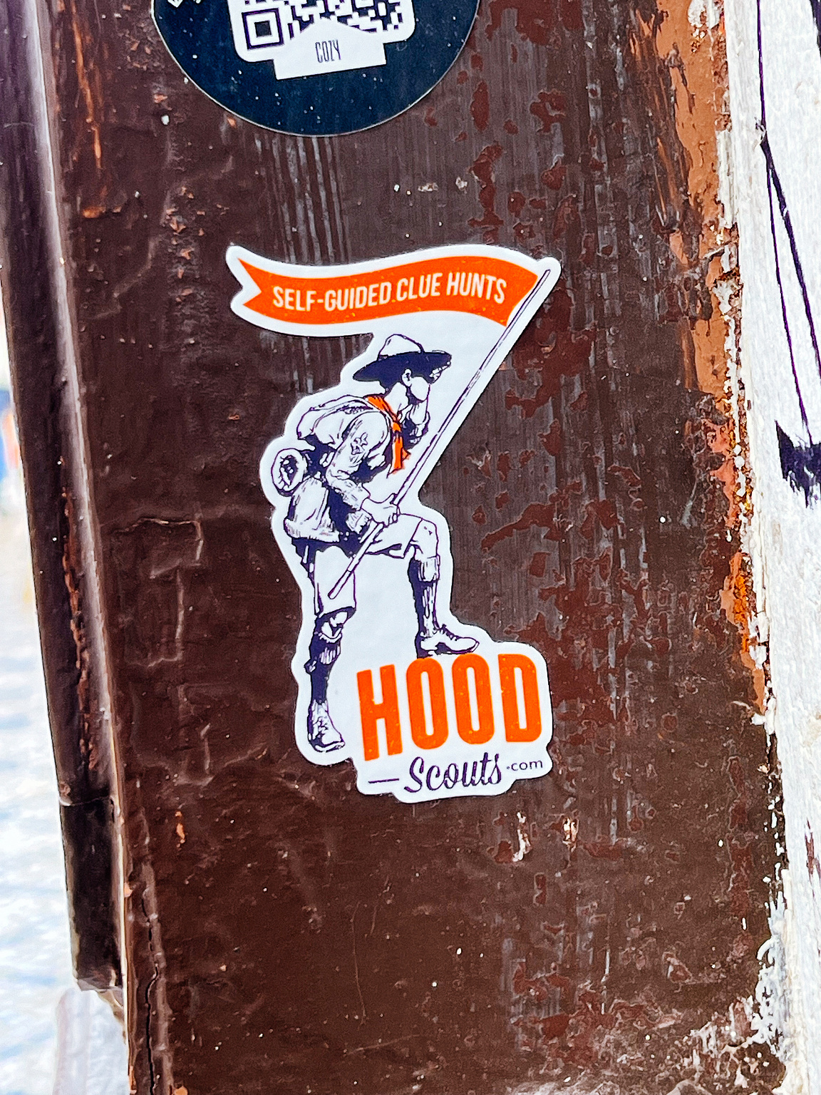 A sticker on a metal post features a character with a backpack, captioned "SELF-GUIDED CLUE HUNTS".