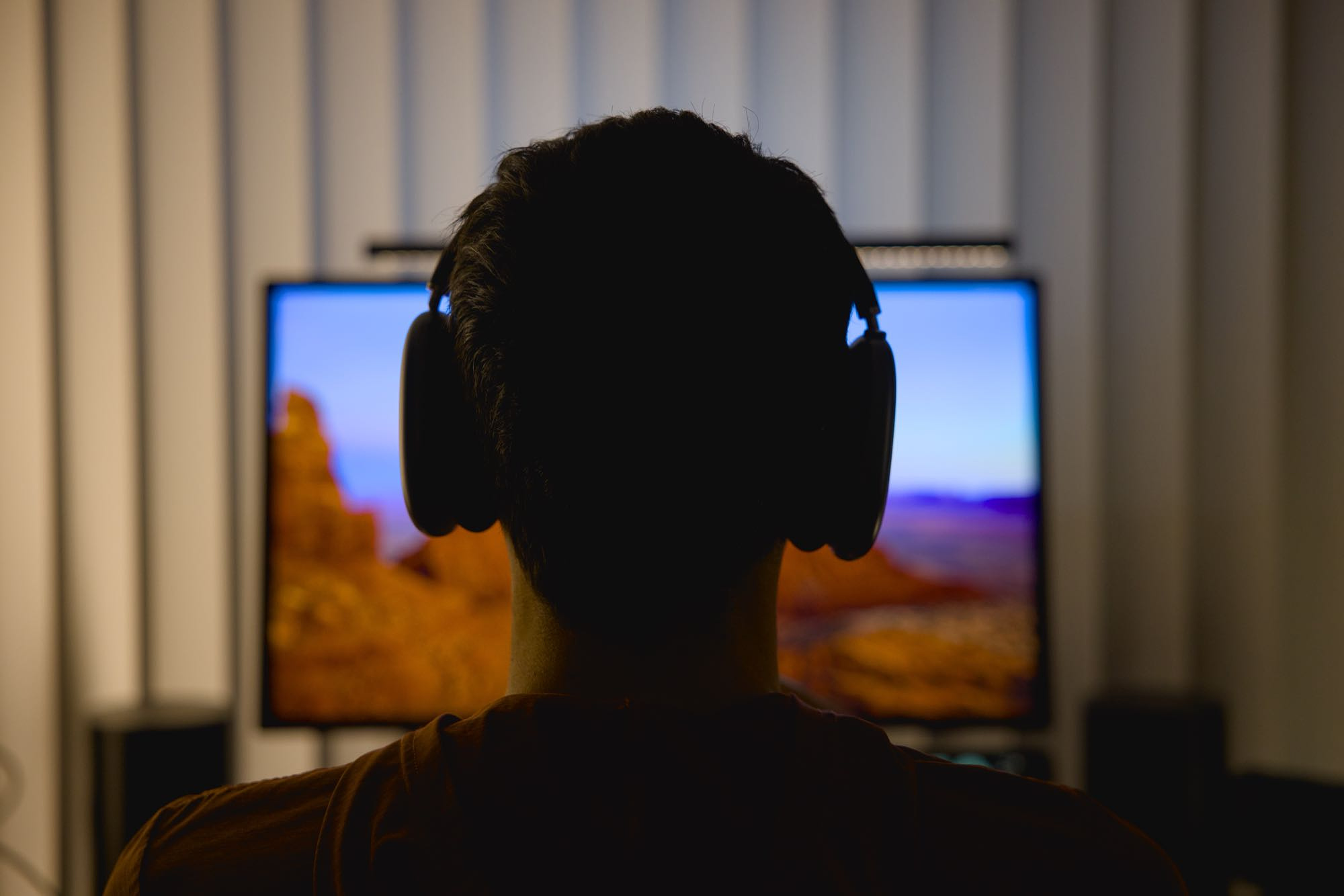 Silhouette of the author, wearing AirPods Max while sitting at his desk, framed by the glow of a monitor.