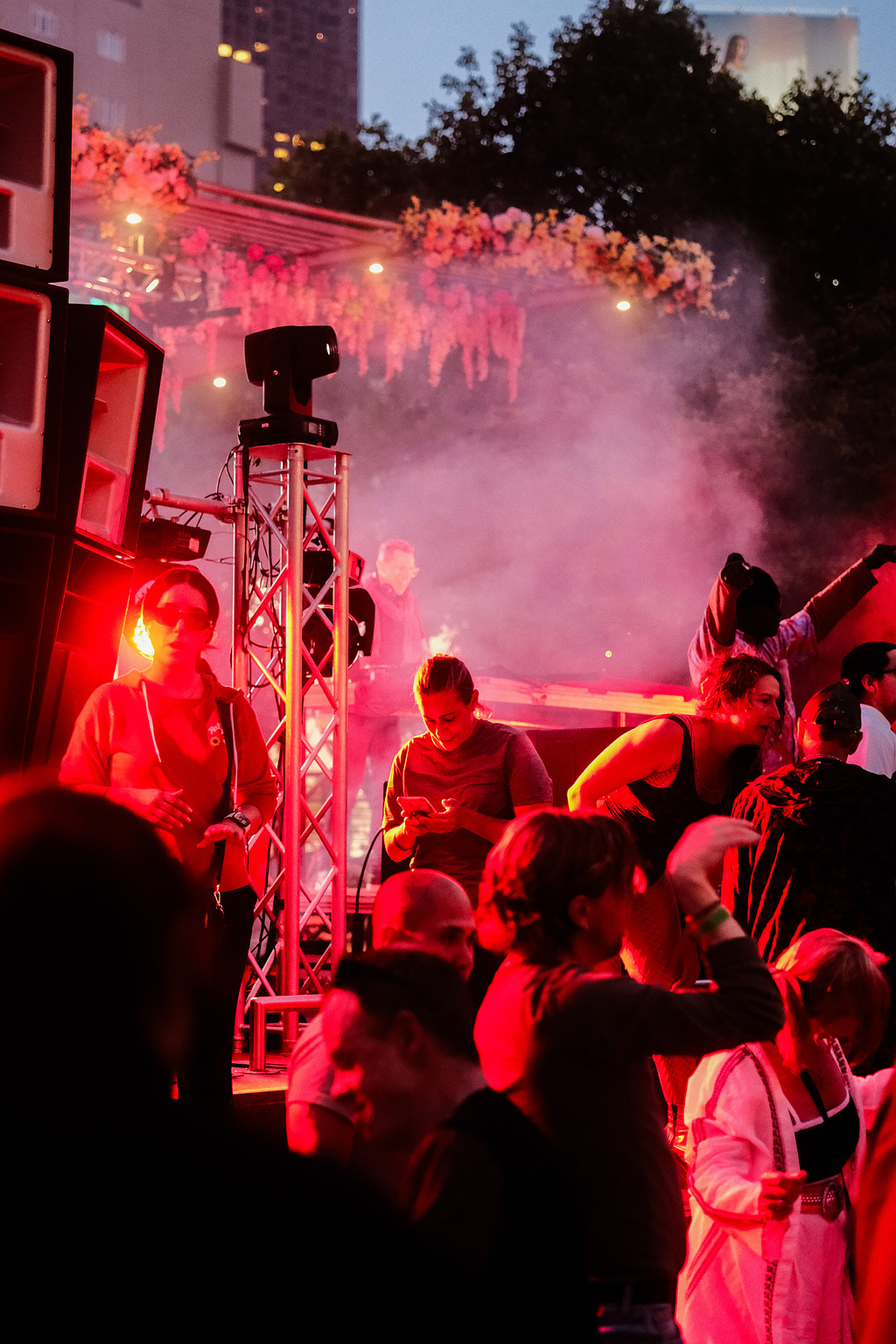 People at an outdoor music event lit in red, fog in the air