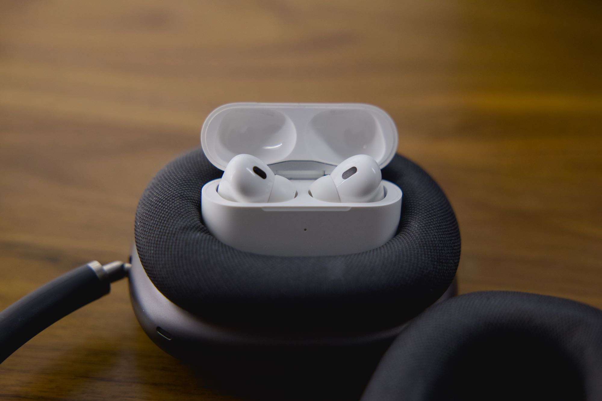 A pair of AirPods Pro 2, with their case open, nestled inside the ear cup of a pair of AirPods Max headphones.