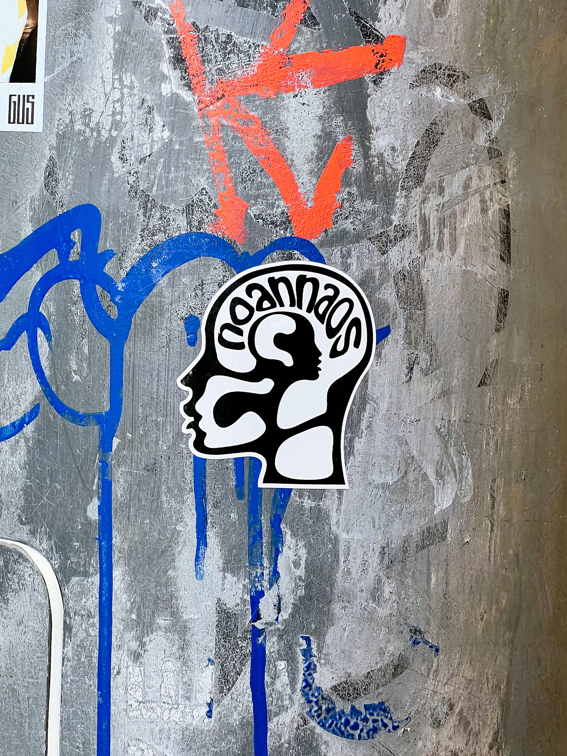 A sticker with a black and white design is placed on a textured surface with blue and orange graffiti.