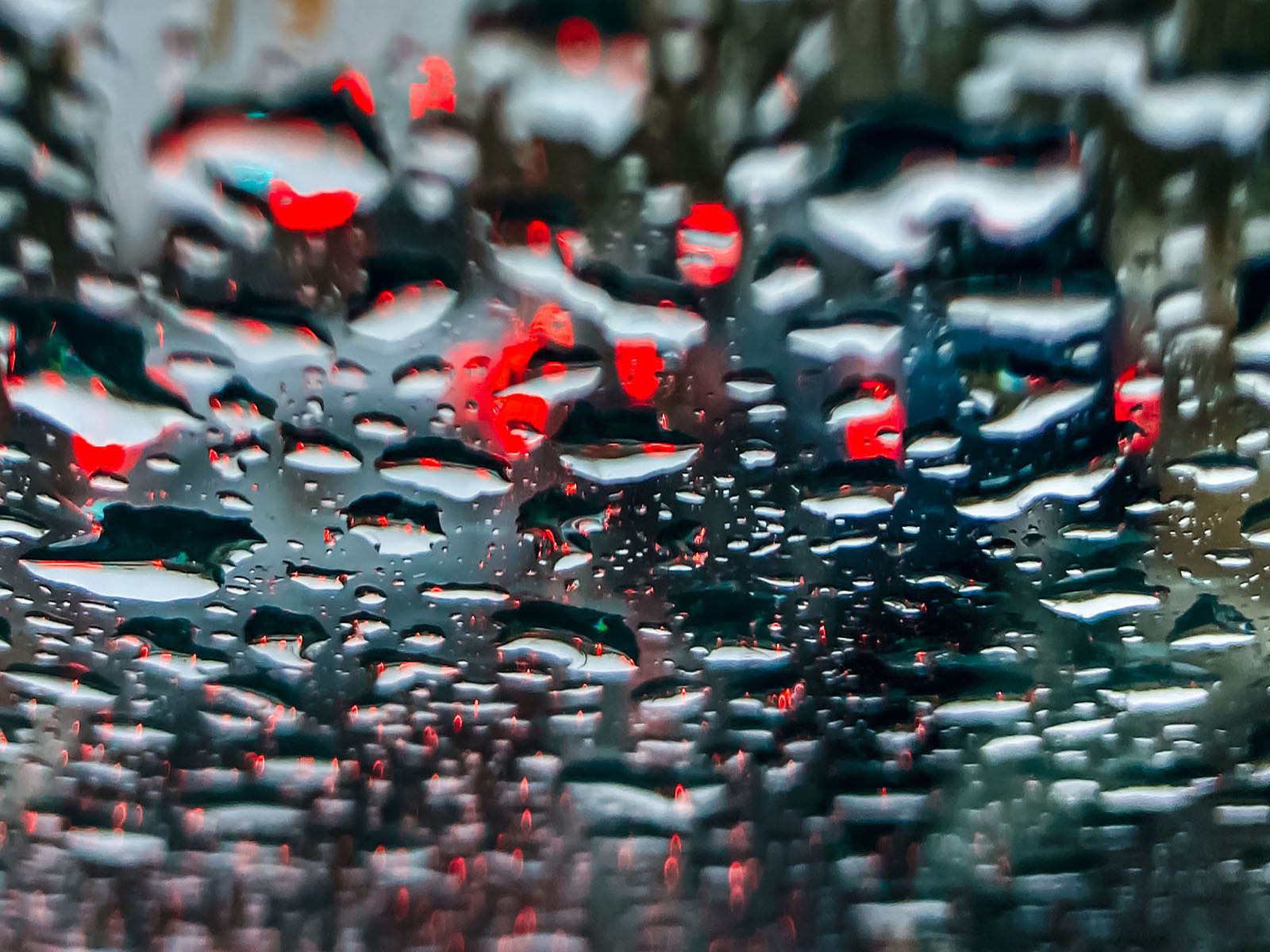 An abstract pattern formed by traffic lights shining through a rain-covered windshield.﻿