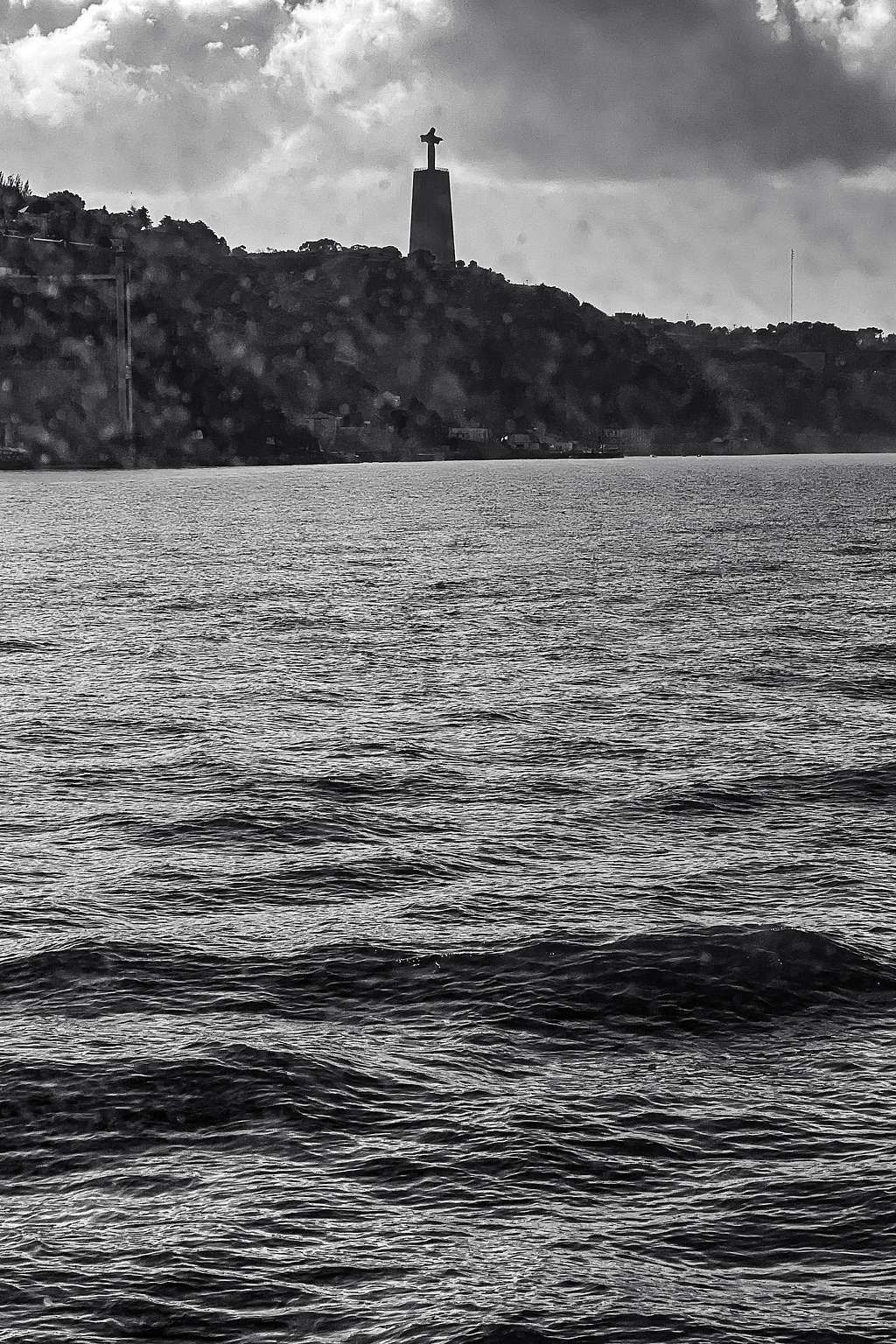 A statue of Christ, up on a hill, seen from a river. 