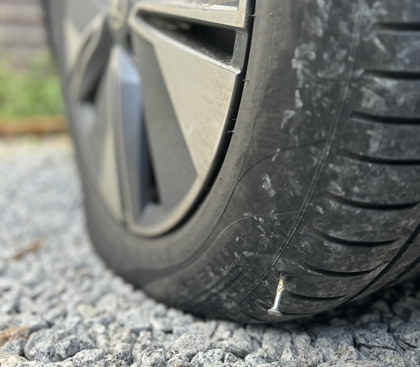 A close-up of a car tyre with a screw embedded in the tread.