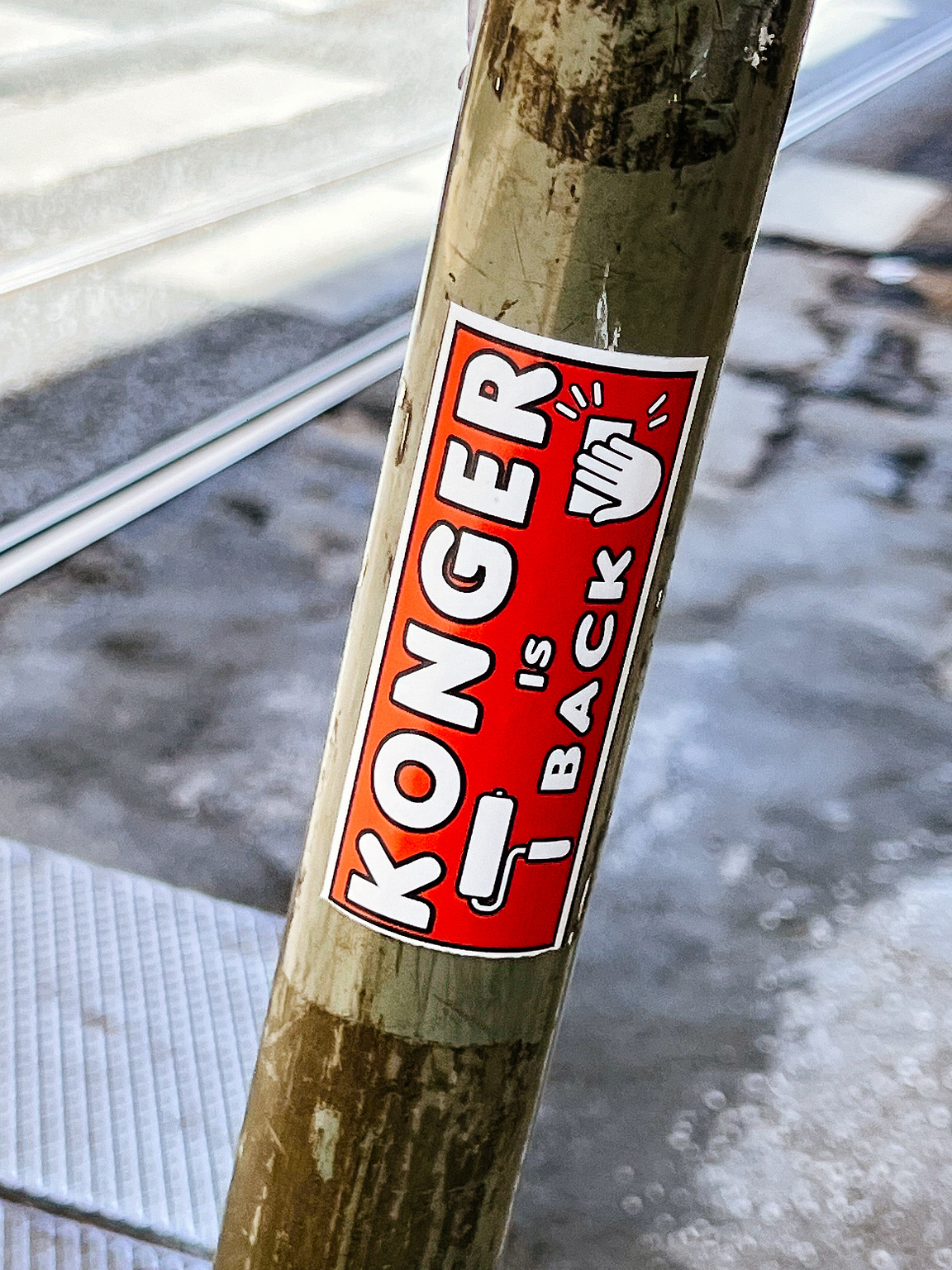 A sticker on a pole with the text "KONGER IS BACK !!!" in bold letters against a red background.