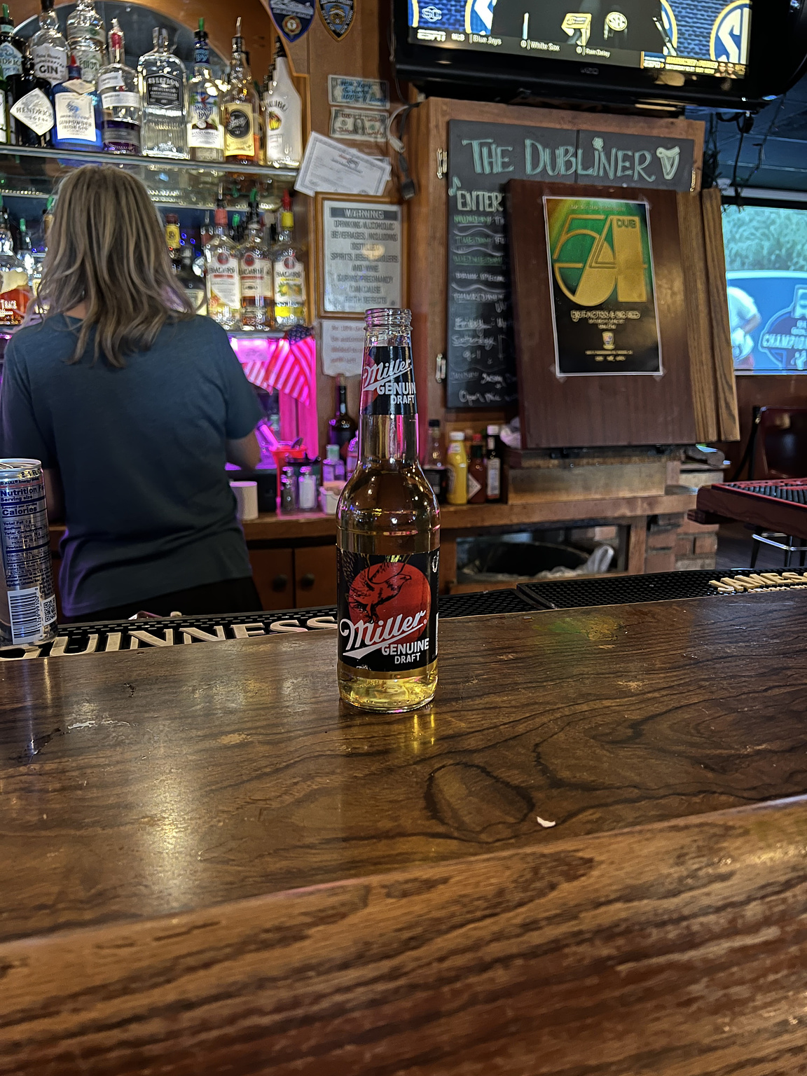 A lone glass of MGD sits on a wooden bar