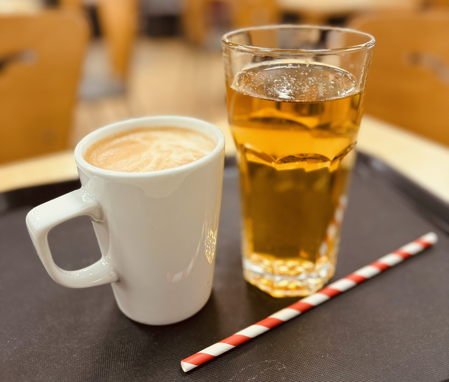 A cup of coffee and a glass of apple juice on a table with a striped straw.