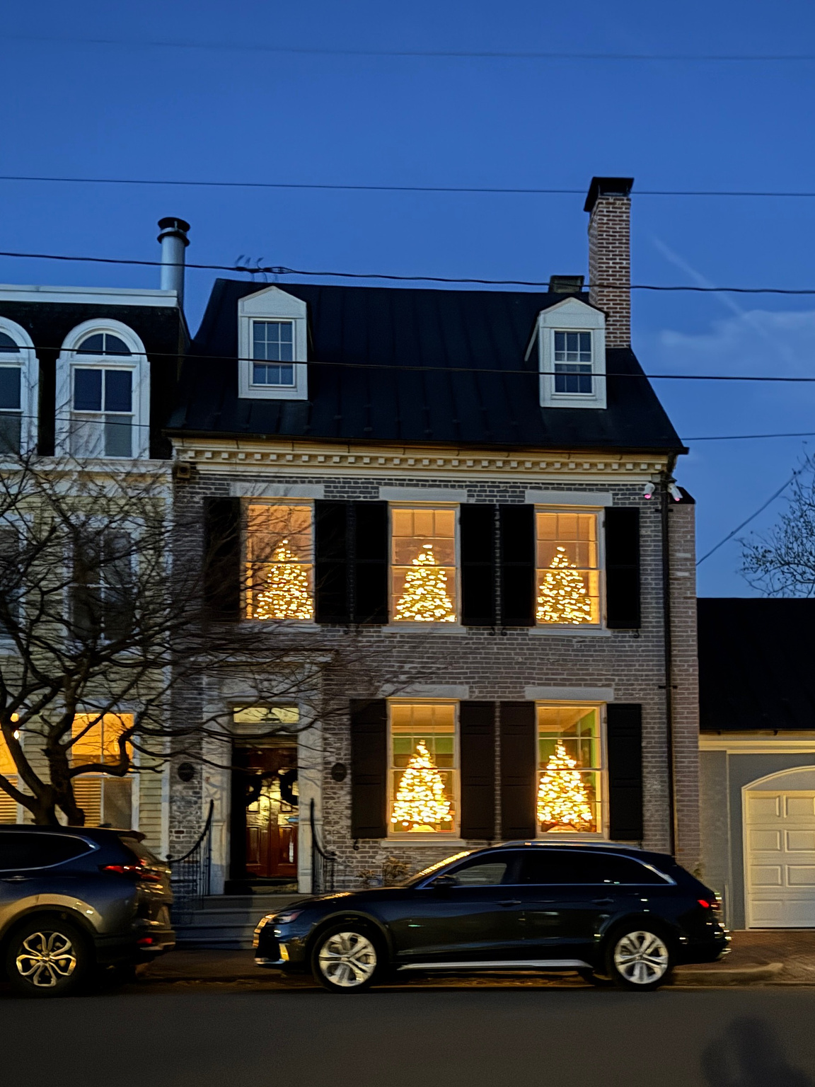 townhome with five windows; three on the second floor, two windows and a door on the first. each window has a Christmas tree lit with white lights