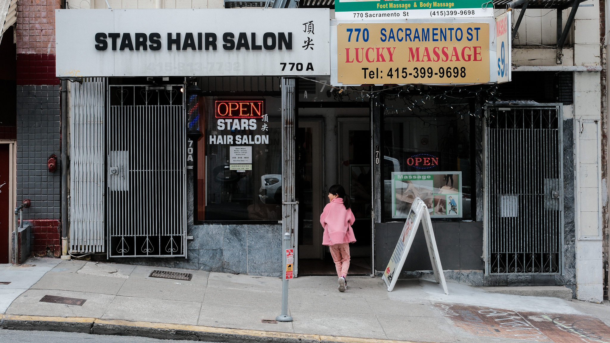 A young girl in pink walks into a hair salon on a Chinatown street. 