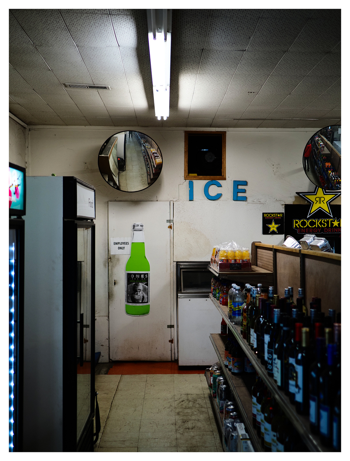 A dimly lit country store aisle. Blue lettering over a walk-in cooler door says "ICE."