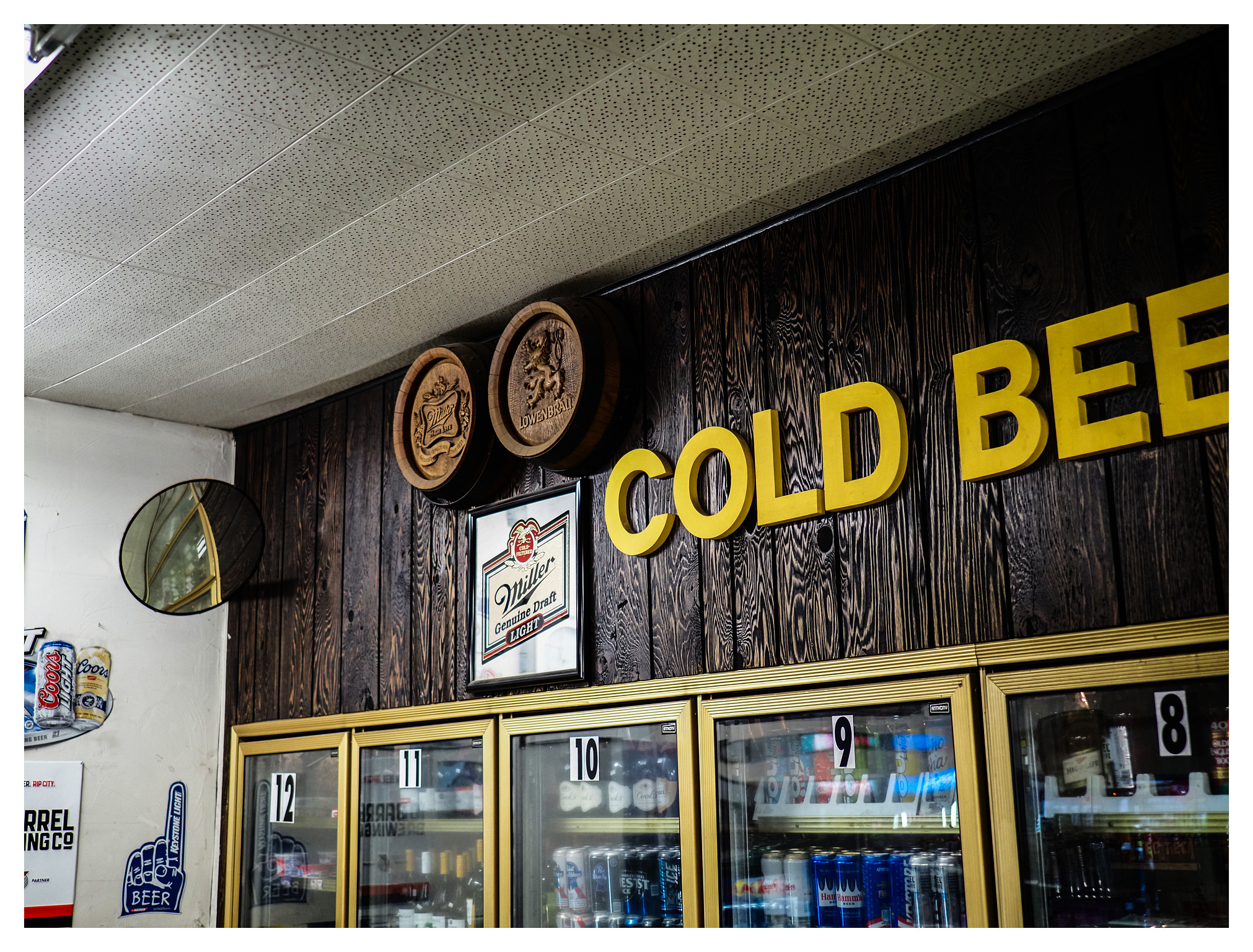 Yellow lettering on faux wood paneling over cooler cases reads "COLD BEER."